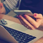 Woman holding mobile by laptop
