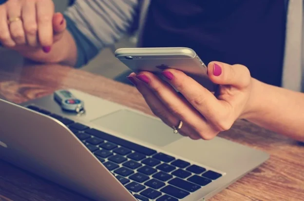 Woman holding mobile by laptop